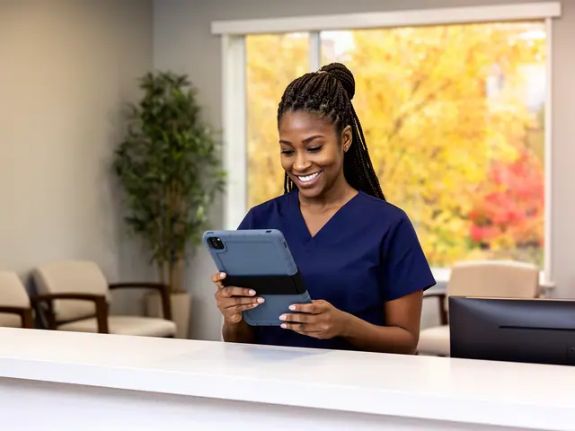 Clinic office manager in navy scrubs smiling at a tablet behind a white front-desk counter